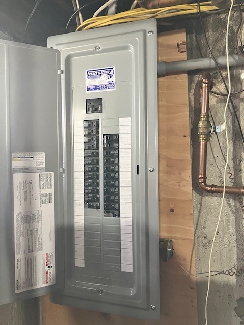 The image shows the interior of an electrical panel with various circuit breakers, switches, and colorful wiring. The components are neatly arranged and organized within the metal cabinet.