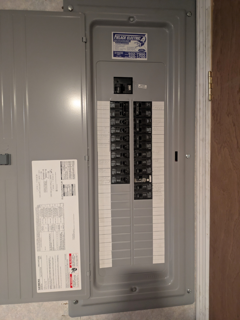 Gray electrical breaker panel features labeled switches and a Fielden Electric sticker on the door.